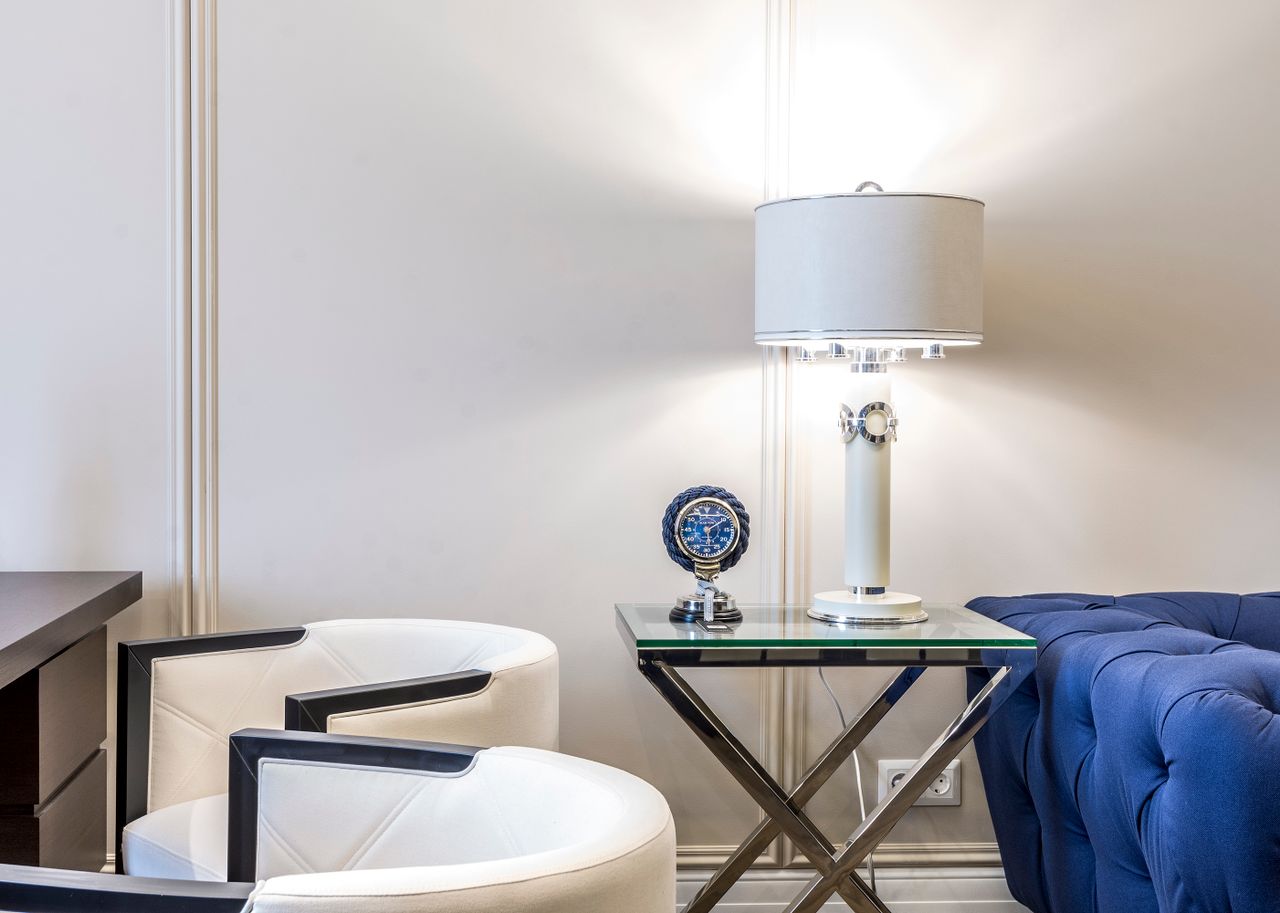 Interior of contemporary living room with small table and lamp near sofa and armchairs